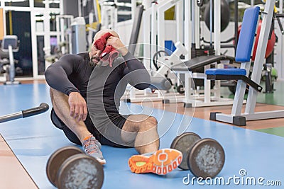 Tired middle aged man sits on a floor after hardworking in gym. Stock Photo