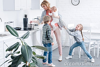 tired mother holding infant child and cooking while naughty children playing Stock Photo