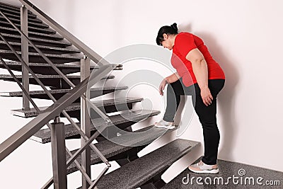Tired overweight mature woman running upstairs indoors Stock Photo