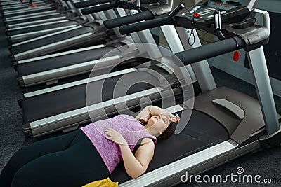 Tired overweight woman lying on treadmill in gym Stock Photo