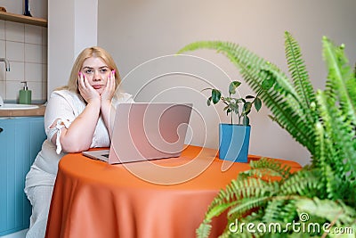 Tired overworked plus size woman sitting in stress or depression at table with laptop. Bored person alone Stock Photo