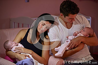 Tired Parents Cuddling Twin Baby Daughters In Nursery Stock Photo