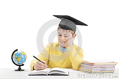 Tired schoolboy does homework sitting at desk. Boy in students hat writing in notebook. Isolation on white background Stock Photo