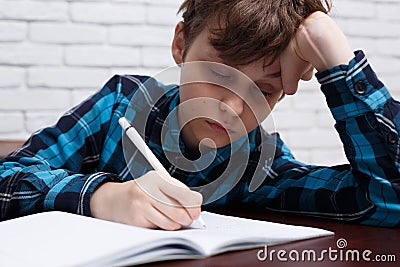 Tired schoolboy falling asleep while studying at copybook. Study Stock Photo