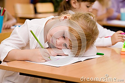 Tired schoolgirl writes in a notebook during lesson Stock Photo
