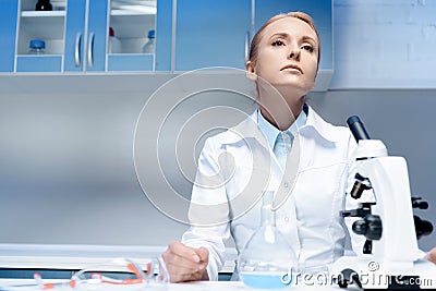 Tired scientist in white coat sitting at workplace in laboratory Stock Photo
