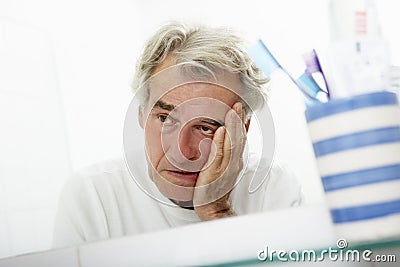 Tired Senior Man Looking At Reflection In Bathroom Mirror Stock Photo