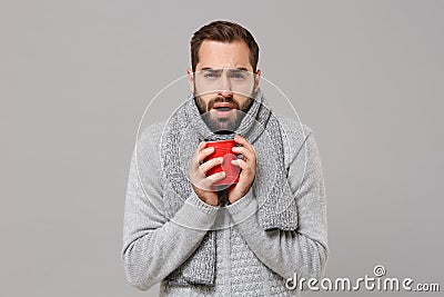 Tired sick young man in gray sweater, scarf posing isolated on grey background, studio portrait. Healthy fashion Stock Photo