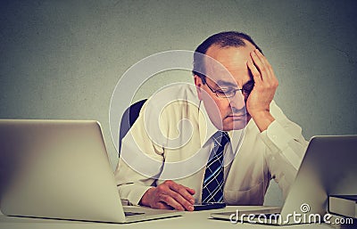 Tired sleepy man sitting at desk with books in front of two laptop computers Stock Photo