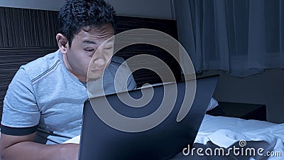 Tired Sleepy Man Working on Laptop untill Midnight on Bed Stock Photo