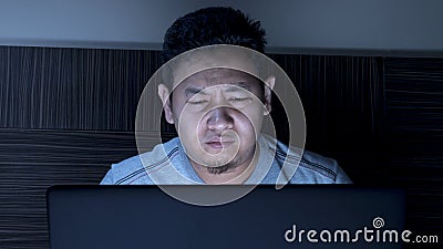 Tired Sleepy Man Working on Laptop untill Midnight on Bed Stock Photo