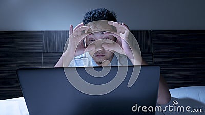 Tired Sleepy Man Working on Laptop untill Midnight on Bed Stock Photo