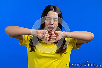 Tired sleepy woman yawns. Girl stretches hands up. Very boring, uninteresting. Blue studio background. Stock Photo