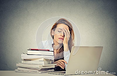 Tired sleepy young woman sitting at her desk with books in front of computer Stock Photo