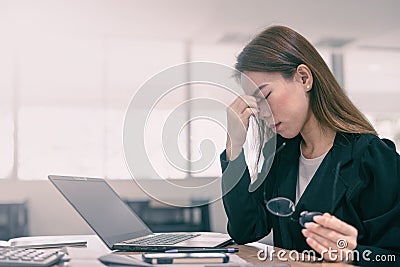 Tired and stressed asian business woman closed eyes massaging nose and sitting at desk in front of laptop at office background Stock Photo