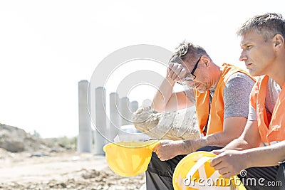 Tired supervisor sitting with colleague at construction site Stock Photo