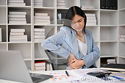 Tired Asian businesswoman suffering from her office syndrome, feeling back pain Stock Photo