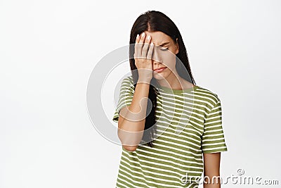 Tired and upset woman facepalm, sighing and feeling sad, standing troubled against white background Stock Photo