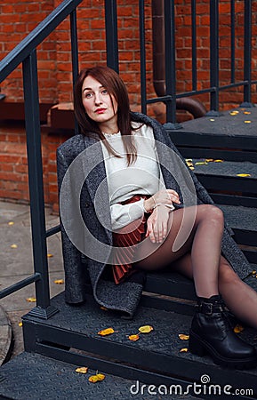 Tired woman in elegant fashionable clothes sitting on a mettalic steps of her house porch. Apathy concept Stock Photo