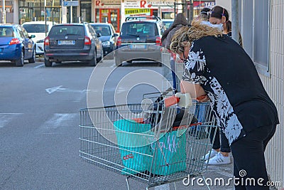 A tired woman with shopping cart. Woman in her 40-ies goes for shopping during pandemic,green bags.Dark shirt Editorial Stock Photo