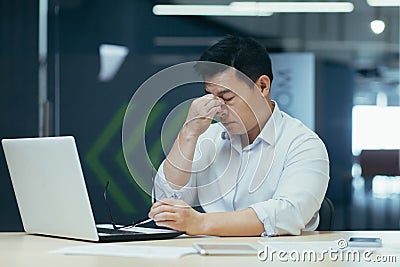 Tired young Asian businessman. Holds his head, feels fatigue and tension in his head Stock Photo
