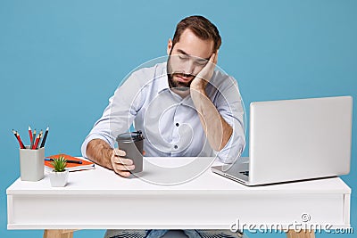 Tired young man in light shirt sit work at desk with pc laptop isolated on blue background. Achievement business career Stock Photo