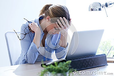 Tired young woman with headache using her laptop at home. Stock Photo