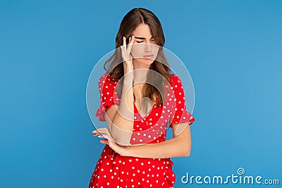 Tired young woman in red dress suffer heavy headache rubbing temples keeping eyes closed over blue background. Stock Photo