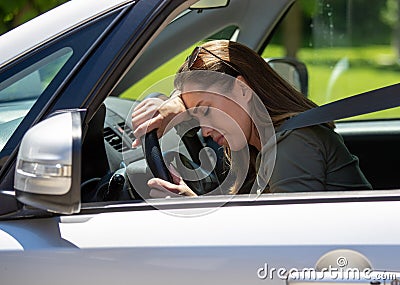 Tired young woman sitting in car leaning on steerin wheel with eyes closed Stock Photo