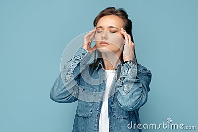 Tired young woman suffer heavy headache rubbing temples keeping eyes closed over blue background. Stock Photo