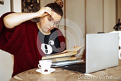 Tired young woman taking off glasses sitting at desk in home room near laptop and reading book. Tiredness from Stock Photo