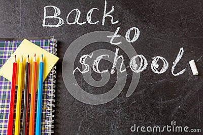 Title Back to school written by white chalk and the the notebook with colorful pencils on the black school chalkboard Stock Photo