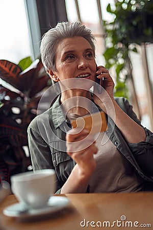 Careful aged woman talking by phone in cafe Stock Photo