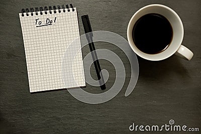 To do list on gridded spiral notepad with cup of coffee, on slate table top - from above, minimal Stock Photo