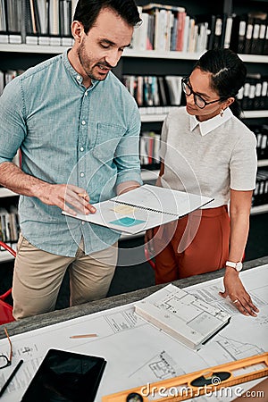 On to the next project. two aspiring young architects looking at a notebook working together in a modern office. Stock Photo