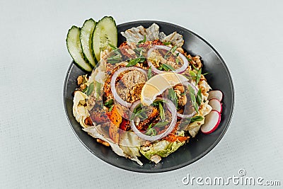 To view closeup of roasted orange bell peppers, onion, radish, lemon and lettuce in a black bowl Stock Photo