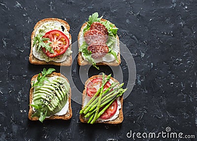 Toast sandwiches with avocado, salami, asparagus, tomatoes and soft cheese on dark background, top view. Tasty breakfast, snack or Stock Photo