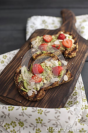 Toasts with avocado and strawberries, on grain bread for breakfast. White napkin with spikes and a black wooden background. Copy Stock Photo