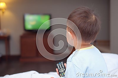 toddler baby boy child sitting in bed holding the tv remote control and watching television Stock Photo