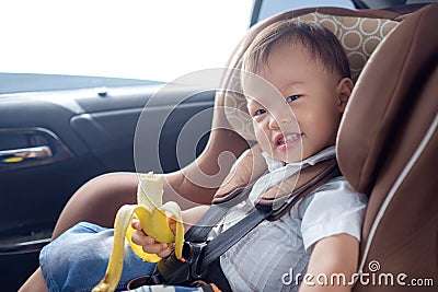 Toddler baby boy child sitting in safety carseat holding & enjoy eating banana Stock Photo