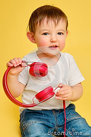 Toddler baby listens to music in red headphones on a studio yellow ba Stock Photo