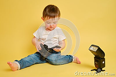 Toddler baby photographer with a camera Canon on a studio yellow ba- Editorial Stock Photo