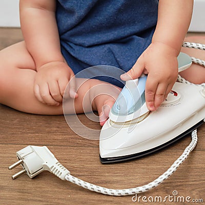 Toddler baby plays with a hot electrical iron. Child boy holding a dangerous iron Stock Photo