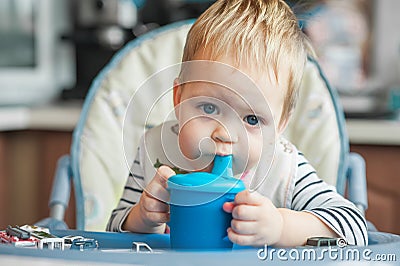 Toddler boy drinks from cup in high chair. Stock Photo