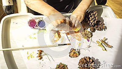 Toddler boy is painting yellow leaves and pine cones in fall with eco friendly paint. Sensorial activity at home Stock Photo