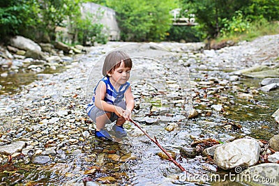 Toddler boy plays with stick in flashy river Stock Photo