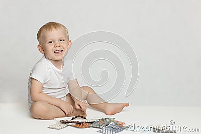A toddler boy sits, laughs and plays with pills on a white background Stock Photo