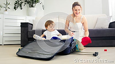 Cute toddler boy sitting in suitcase while mother packing things in suitcase for holiday Stock Photo