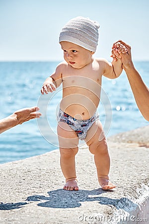 Toddler boy walking on stone pier looks incredulously at woman Stock Photo