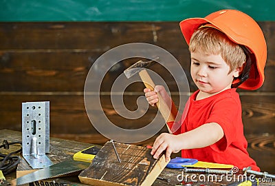 Toddler on busy face plays with hammer tool at home in workshop. Child in helmet cute playing as builder or repairer Stock Photo